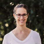 Eine junge Frau mit dunklen Haaren und Brille lächelt