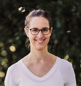 Eine junge Frau mit dunklen Haaren und Brille lächelt