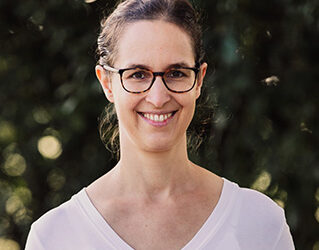 Eine junge Frau mit dunklen Haaren und Brille lächelt