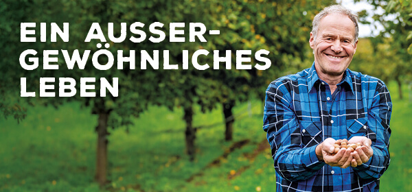Ein lächelnder Mann im blau-schwarz-karierten Hemd hält einige Haselnüsse in seiner Hand